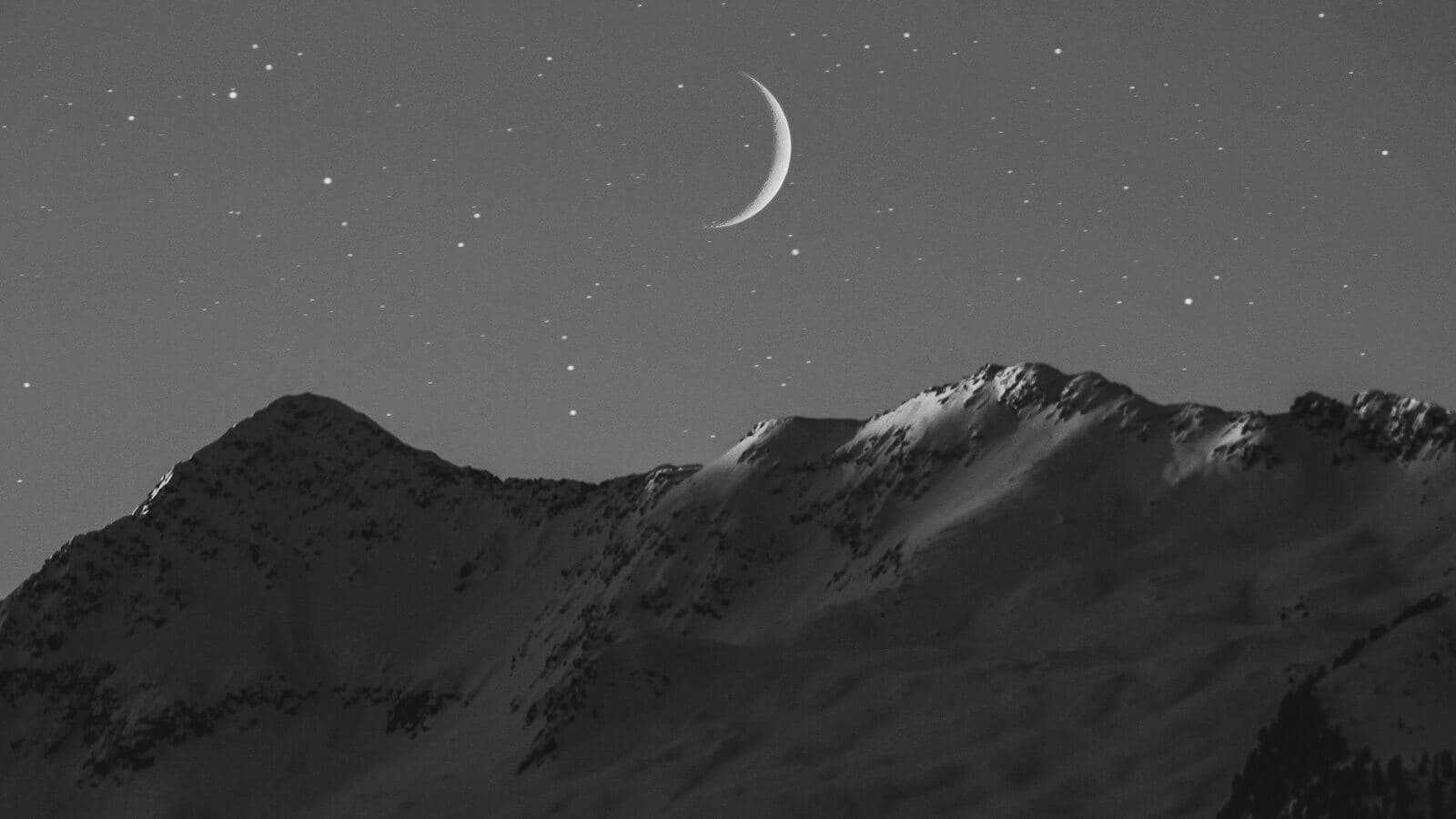 A crescent moon over a snowy mountain