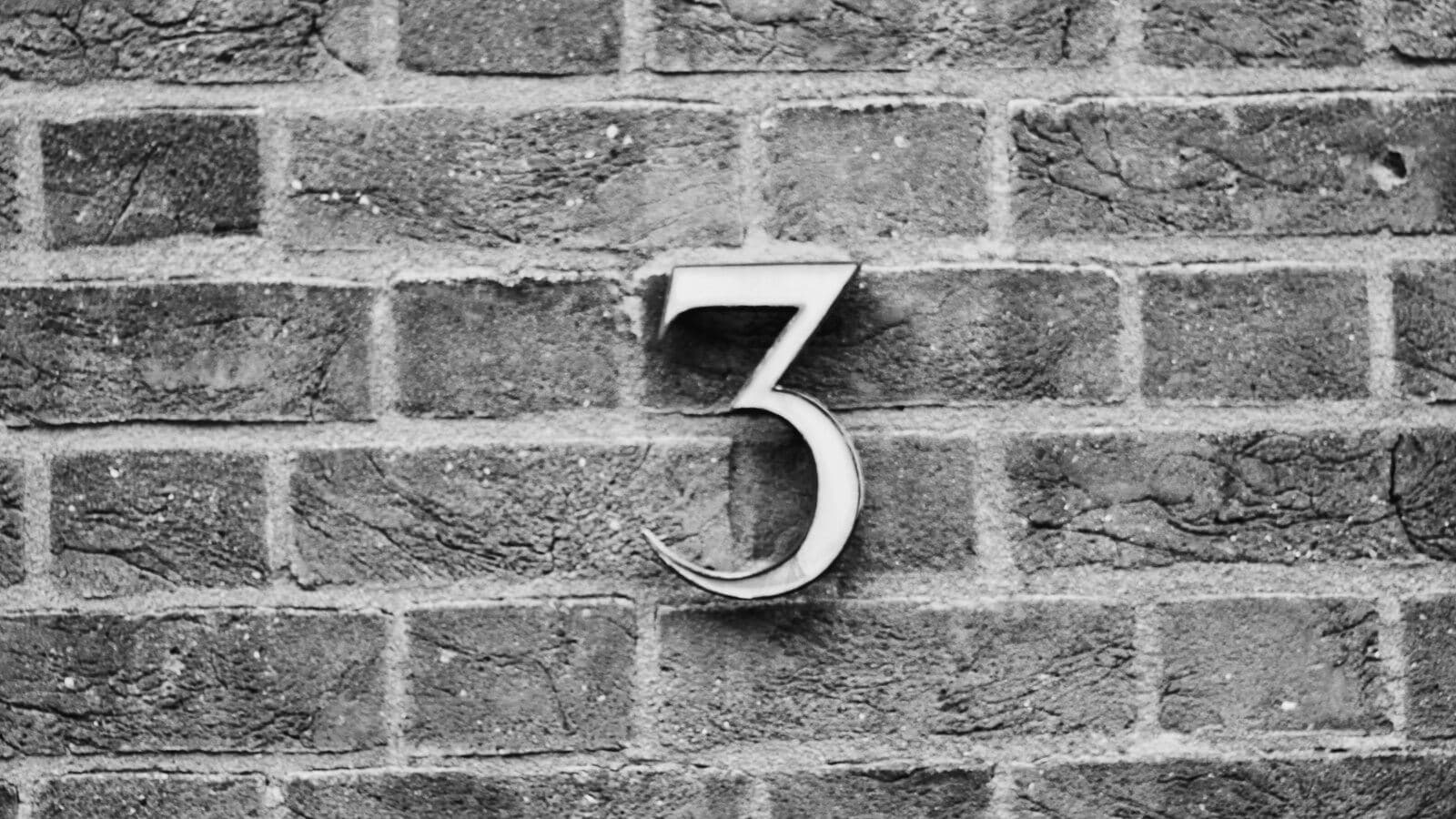 Un número 3 metálico sobre una pared de ladrillo