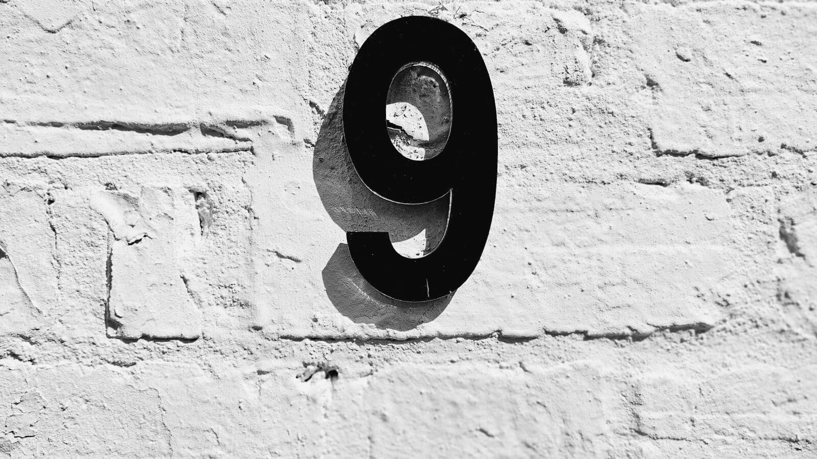 A black number 9 on a white brick wall